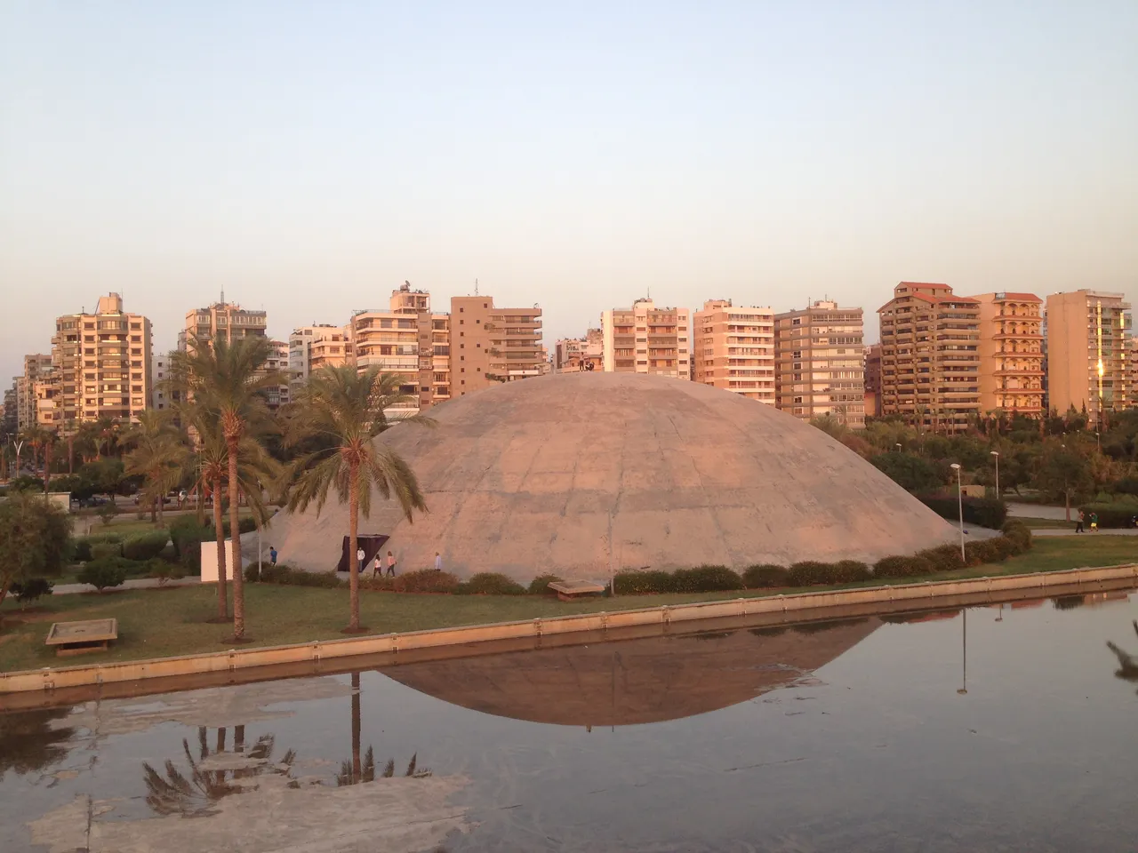 Oscar Niemeyer's concrete dome at the Tripoli fair, reflected in a pool at golden hour