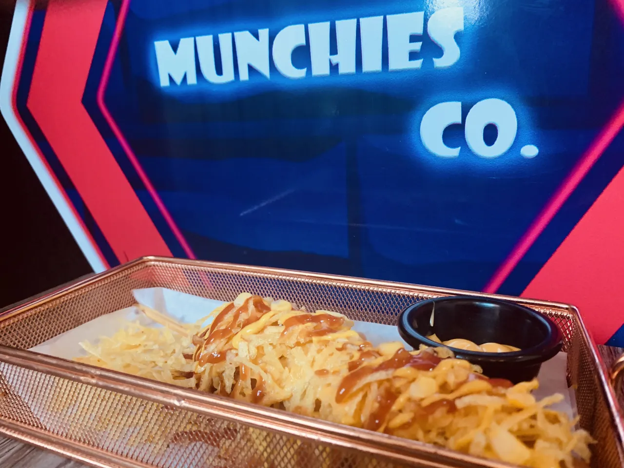 A basket of loaded fries under the neon Munchies Co sign