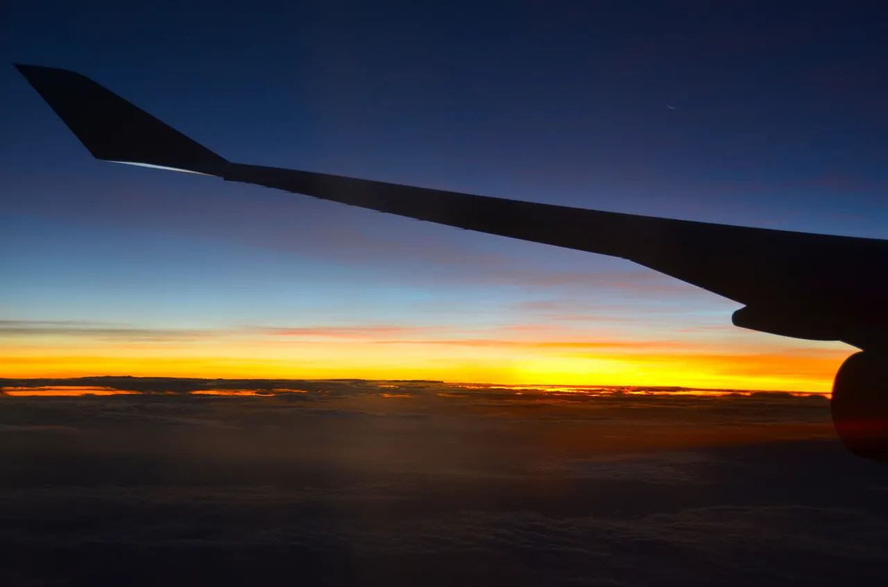 An airplane wing above the clouds at sunset