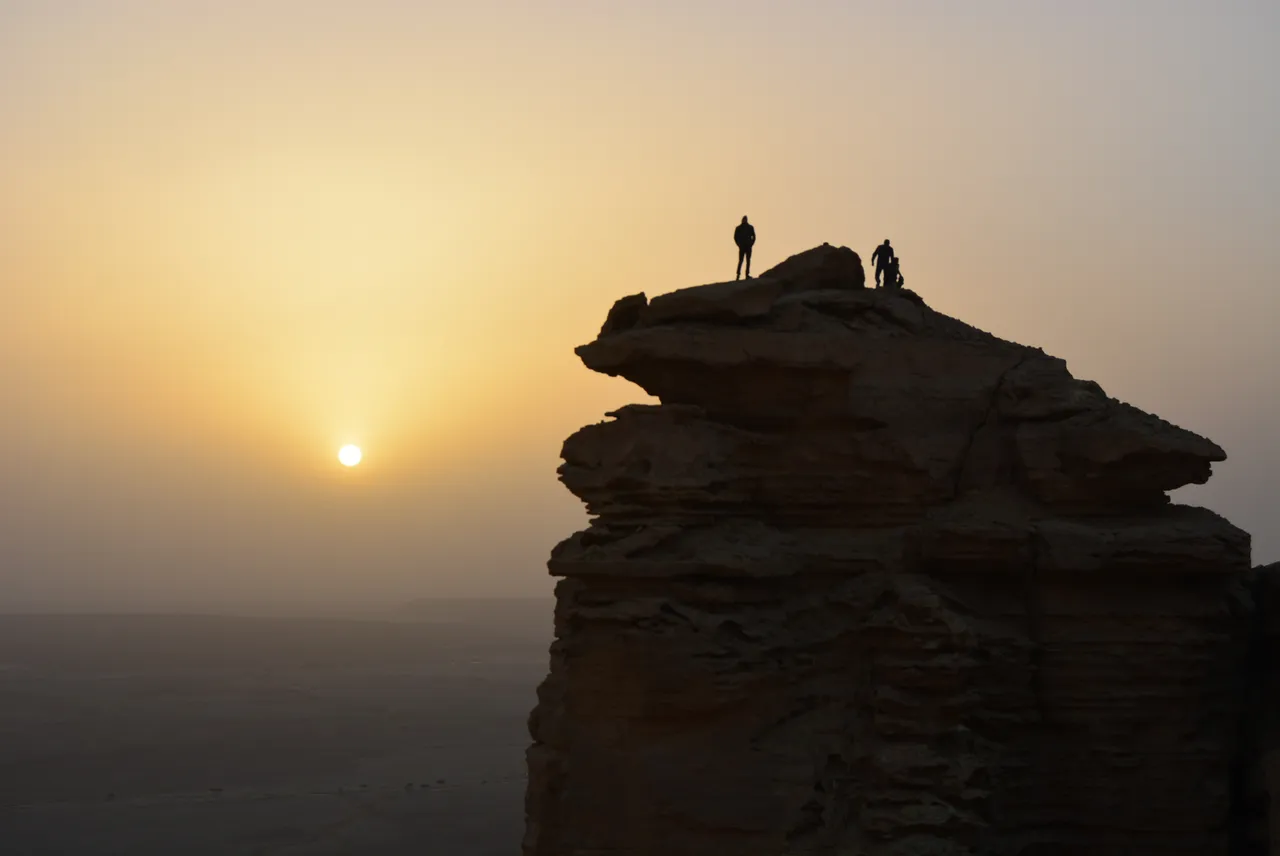 Two hikers on a rock outcrop at the Edge of the World near Riyadh at sunset